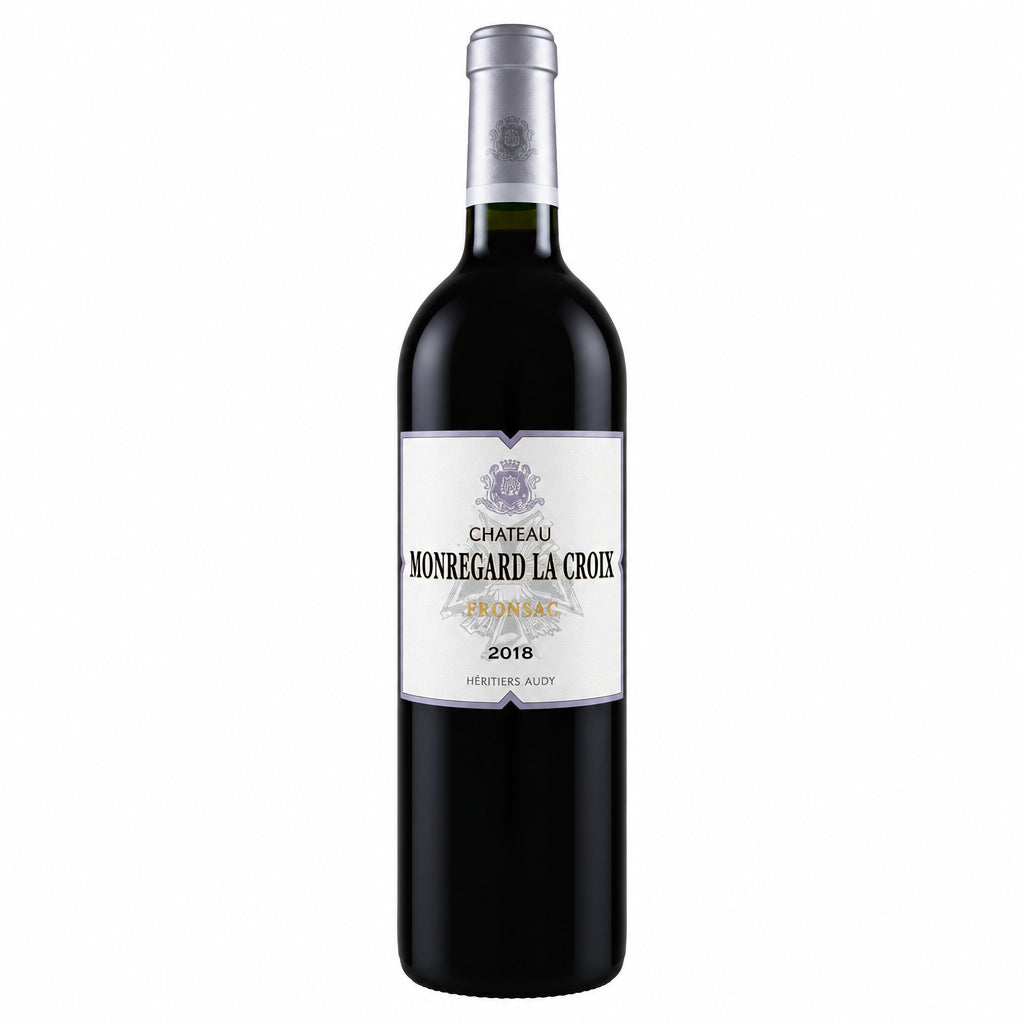 Bottle of Chateau Monregard La Croix 2018 red wine with a dark label and cork, standing upright on a wooden surface.