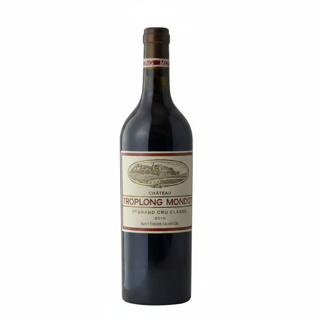 Bottle of Chateau Troplong Mondot 2016 red wine with a dark label, placed on a wooden surface against a blurred vineyard background.